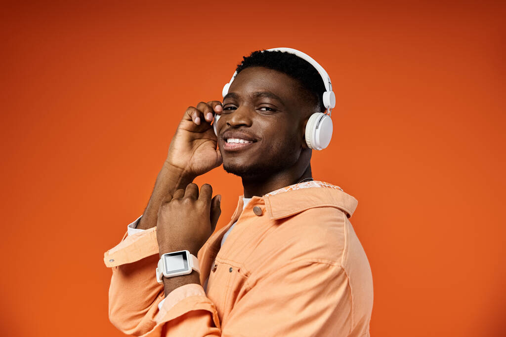 Fajny, stylowy młody czarny mężczyzna pozowanie ze słuchawkami na żywe pomarańczowe tło. - Zdjęcie, obraz