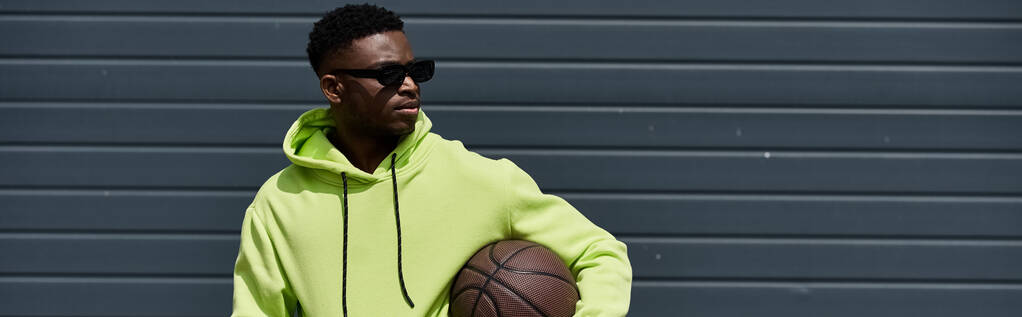 Schöner afroamerikanischer Mann in grünem Kapuzenpullover hält Basketball. - Foto, Bild