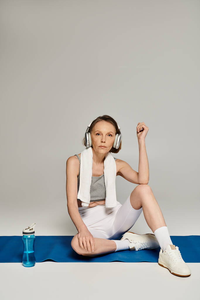 Een volwassen vrouw, versierd met een koptelefoon, zit op een yoga mat in een serene houding. - Foto, afbeelding