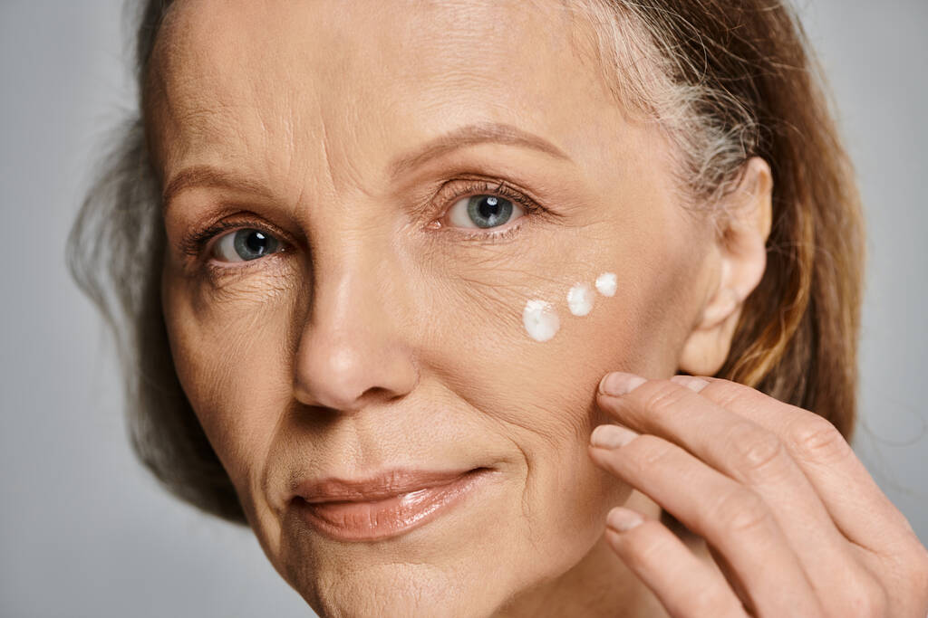 Una mujer con gracia se aplica crema en la cara. - Foto, imagen
