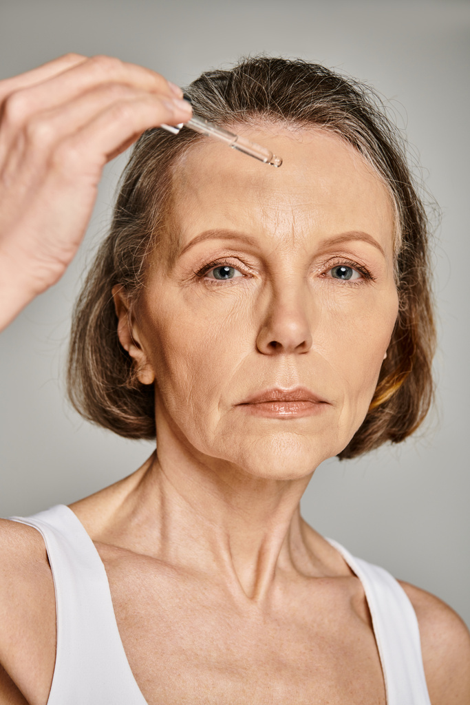 Een vrouw brengt zorgvuldig een serum aan op haar gezicht, gericht op haar huidverzorgingsroutine. - Foto, afbeelding
