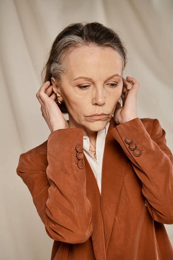 Mujer madura en chaqueta bronceada posa con gracia con las manos en las orejas. - Foto, imagen