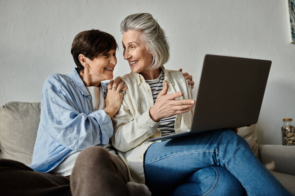 Дві літні жінки діляться ноутбуком на затишному дивані. - Фото, зображення