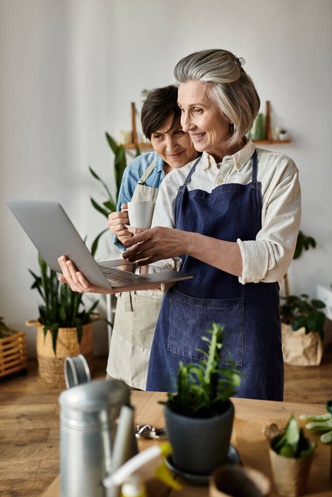 Két idősebb nő, akik laptoppal vannak elfoglalva a hangulatos konyhában.. - Fotó, kép