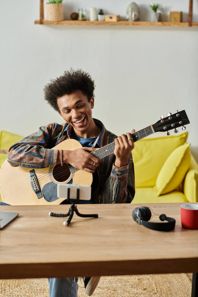 A man strums an acoustic guitar in front of a phone, creating music for an online audience. - Foto, afbeelding