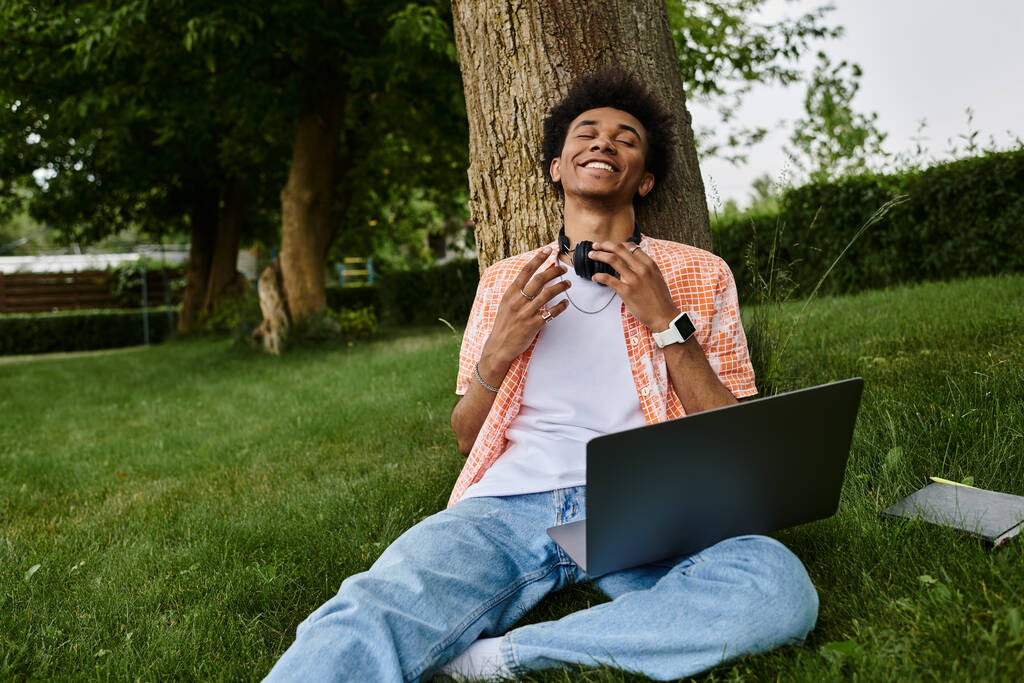 Young african american man sitting on grass, using laptop. - Foto, imagen