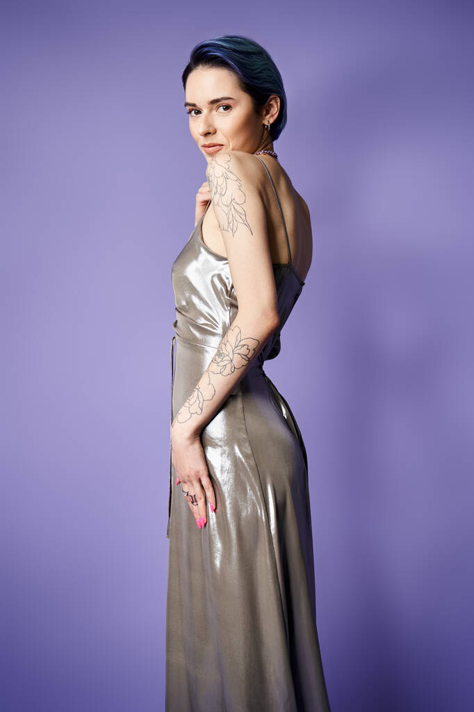A young woman with short blue hair striking a glamorous pose in a shiny silver dress in a studio setting. - Фото, изображение