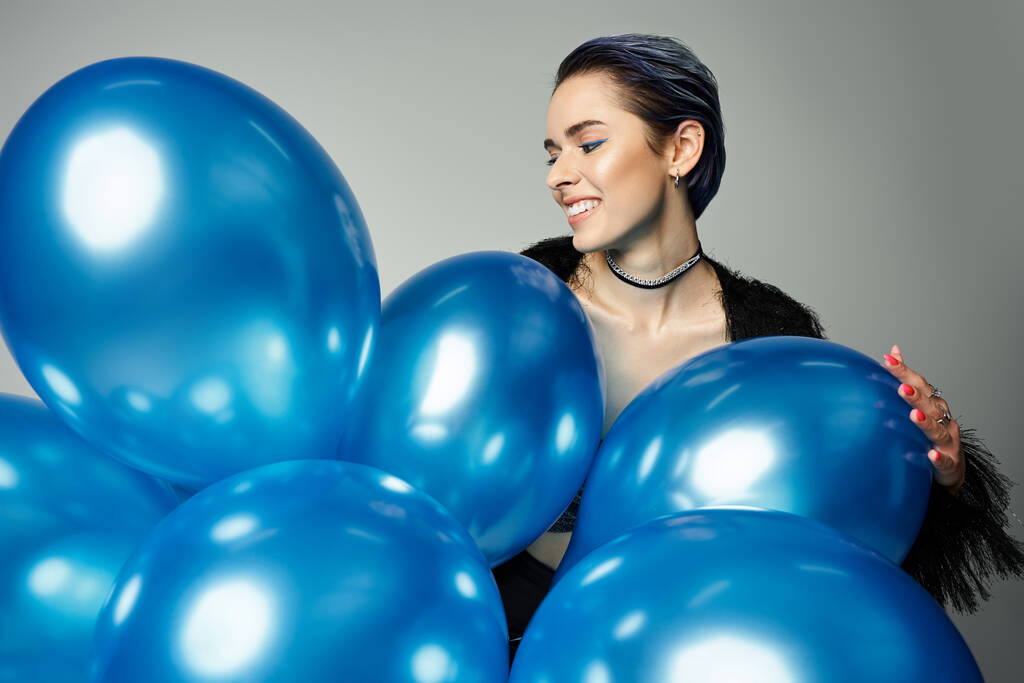 A pretty young woman with short dyed hair poses in stylish attire while holding a bunch of blue balloons. - Foto, immagini
