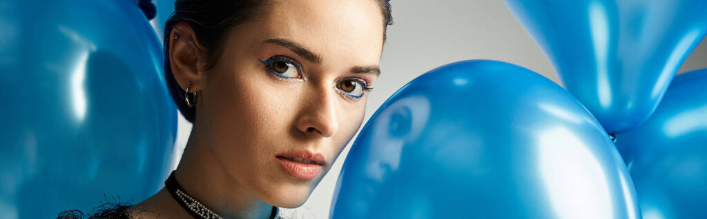 A stylish young woman with short dyed hair holds a collection of beautiful blue balloons in a studio setting. - Zdjęcie, obraz