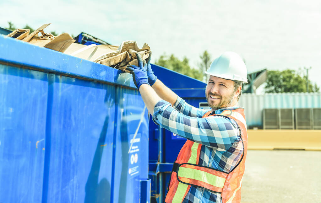 Ein Arbeiter, der Karton auf dem Recyclinghof recycelt - Foto, Bild
