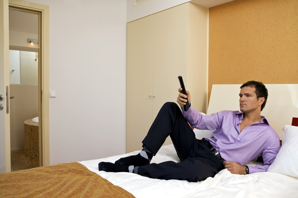 Man op bed houden afstandsbediening - Foto, afbeelding