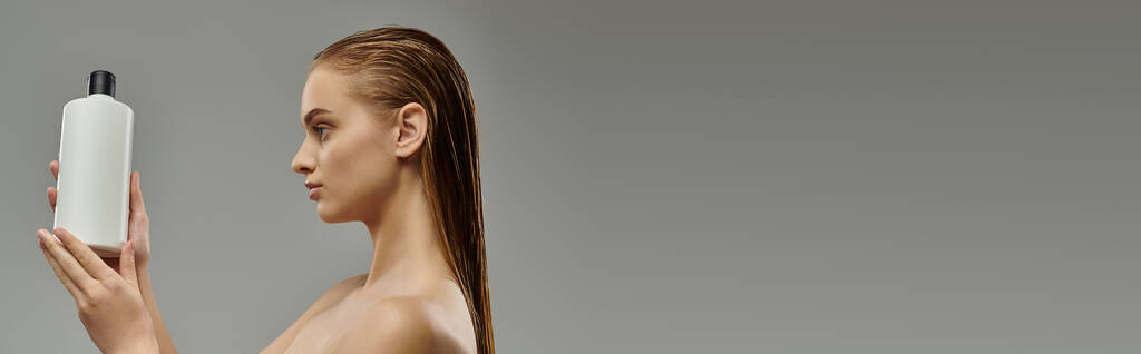 Genç bir kadın bir şişe saç bakım ürünü tutuyor, ıslak saçlarıyla güzellik gösterisini sergiliyor.. - Fotoğraf, Görsel