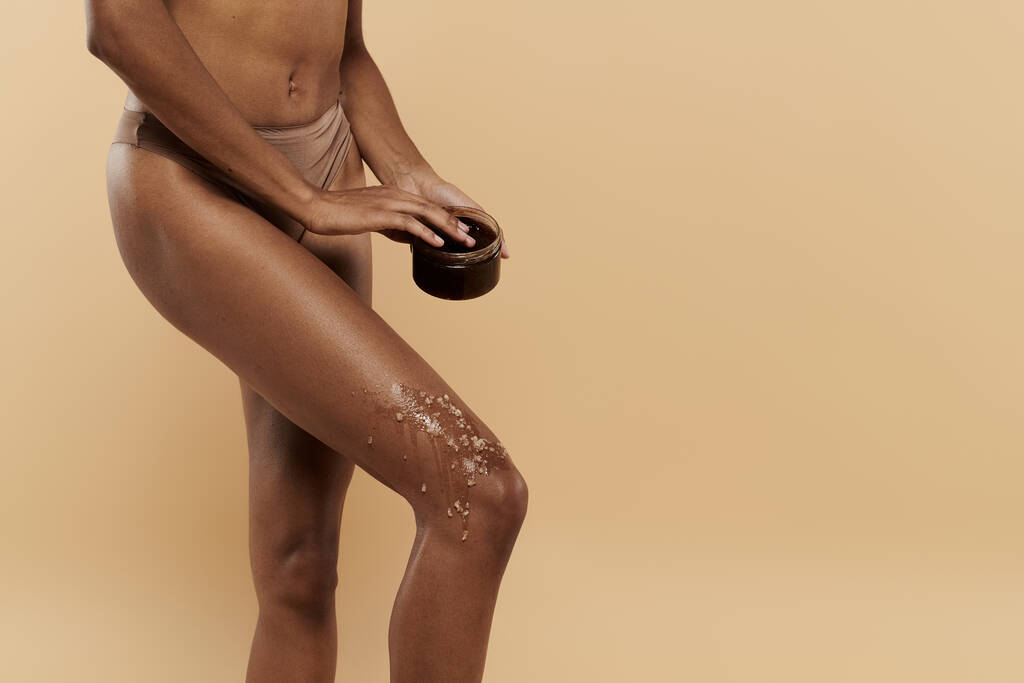 Stylowa Afroamerykanka o szczupłej sylwetce z zarostem do kawy na nogach na beżowym tle. - Zdjęcie, obraz