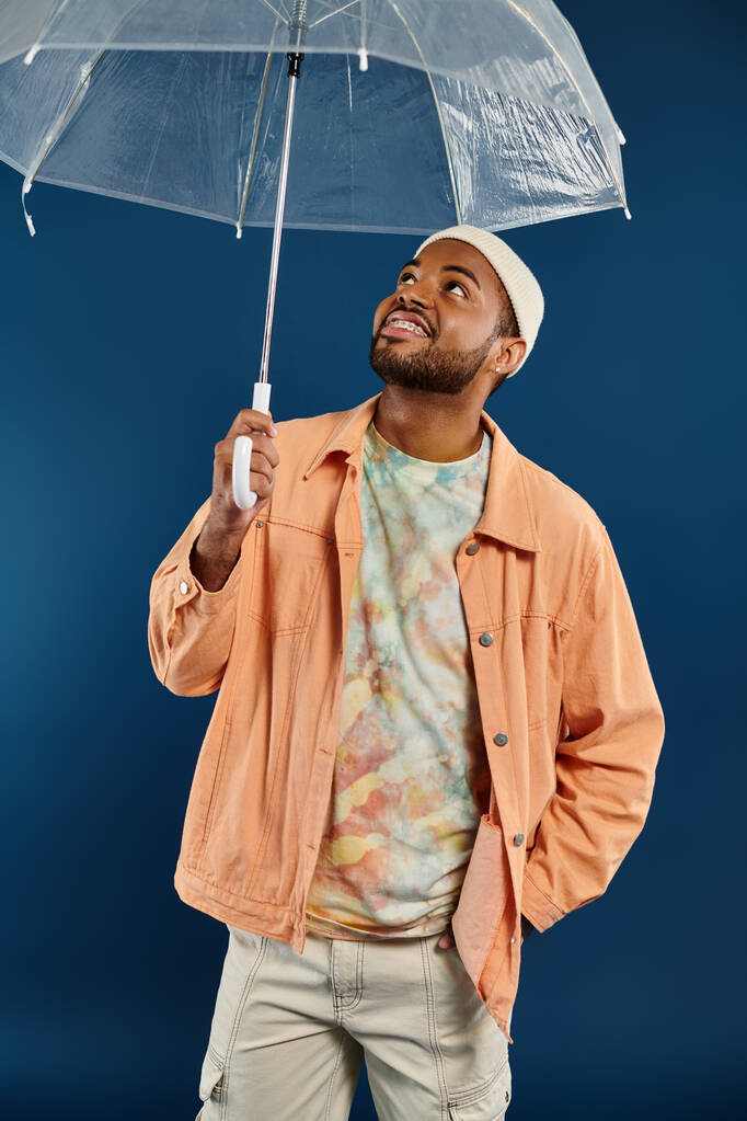 Афроамериканец держит прозрачный зонтик на ярком фоне. - Фото, изображение