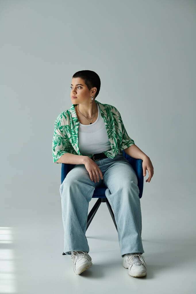 Eine junge Frau mit kurzen Haaren sitzt anmutig auf einem lebhaften blauen Stuhl, entspannt und ruhig.. - Foto, Bild