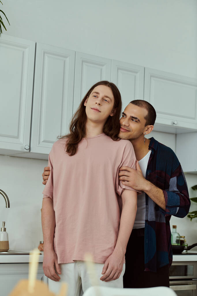 Ένα κομψό γκέι ζευγάρι σε casual ενδυμασία, απολαμβάνοντας ποιοτικό χρόνο στη σύγχρονη κουζίνα τους στο σπίτι. - Φωτογραφία, εικόνα