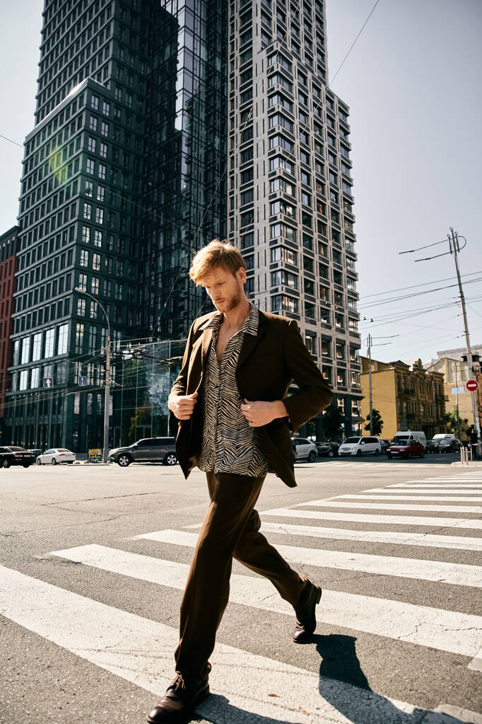 Mladý rusovlasý muž v kostýmech kráčející přes ulici města s vysokými budovami v pozadí. - Fotografie, Obrázek