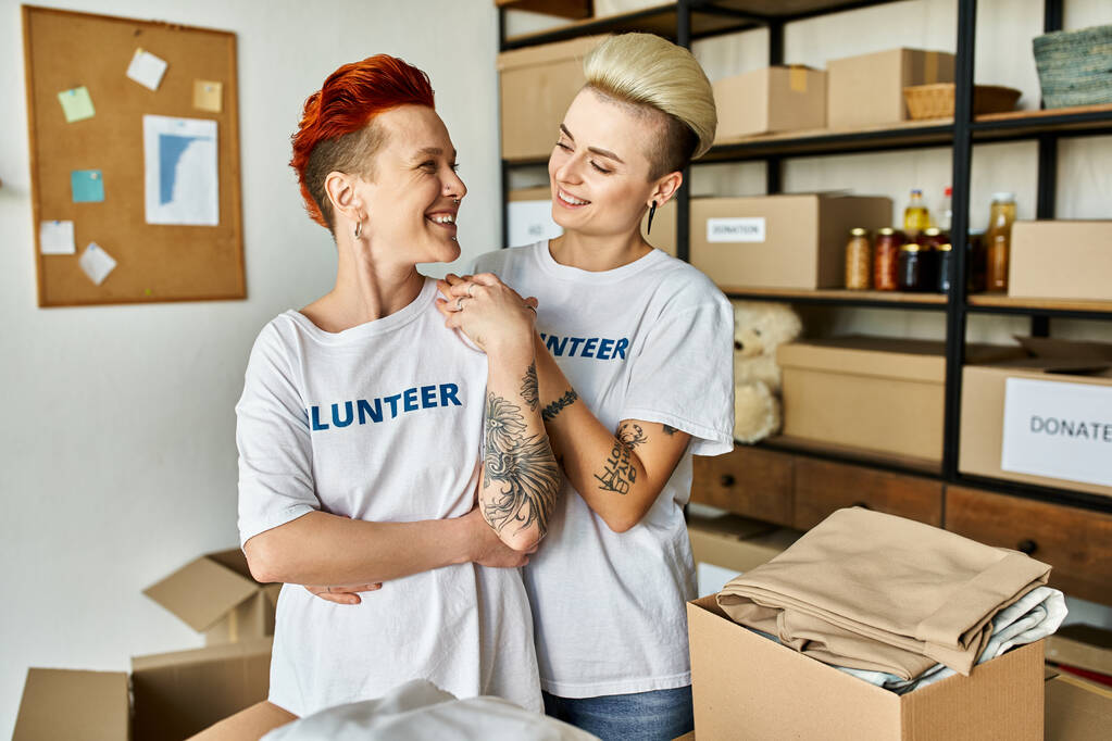 Lesbijska para w ochotniczych koszulkach pracuje razem w organizacji charytatywnej. - Zdjęcie, obraz
