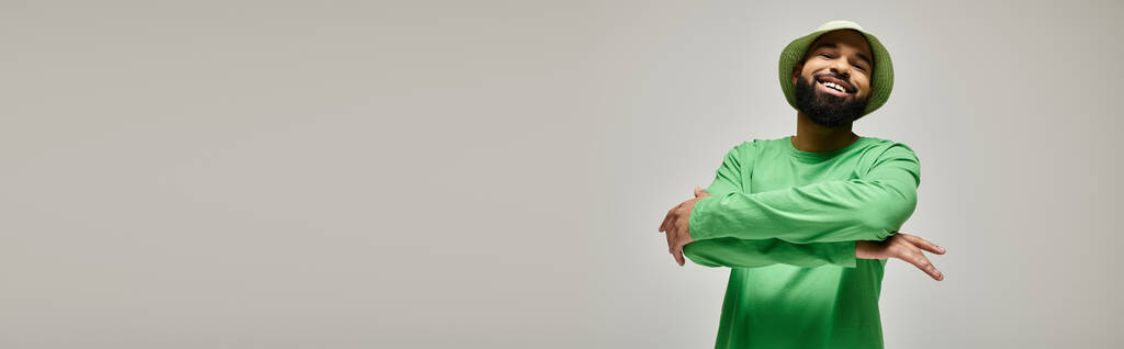 Όμορφος Αφροαμερικανός με πράσινο πουκάμισο και ασορτί καπέλο ποζάρει σε ένα ζωντανό σκηνικό. - Φωτογραφία, εικόνα