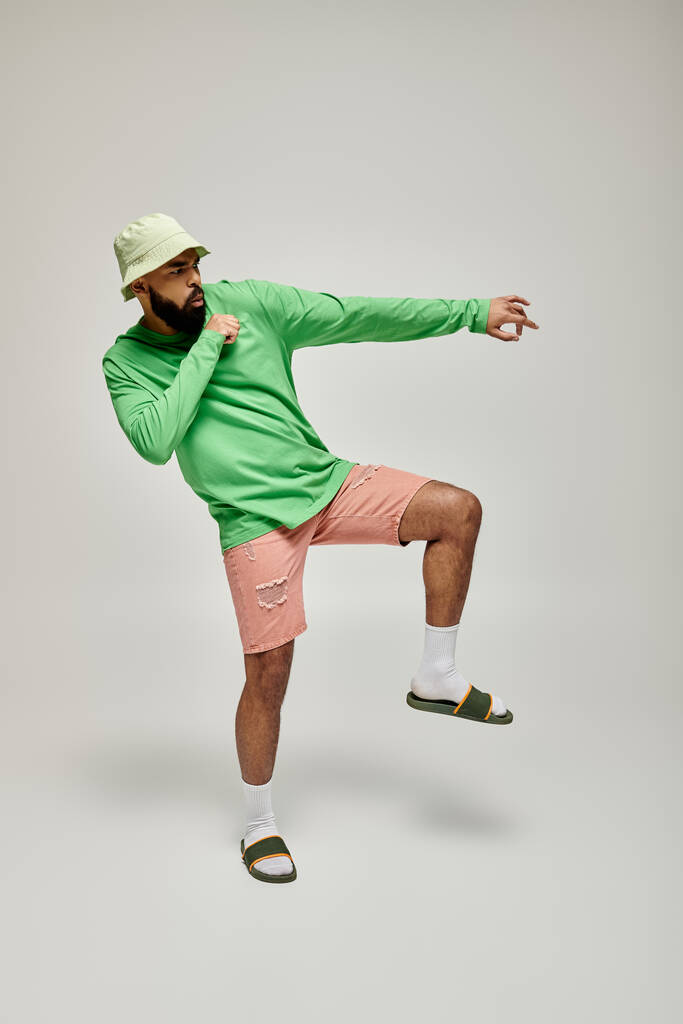 Красивый афроамериканец позирует в модной зеленой рубашке и розовых шортах на ярком фоне. - Фото, изображение