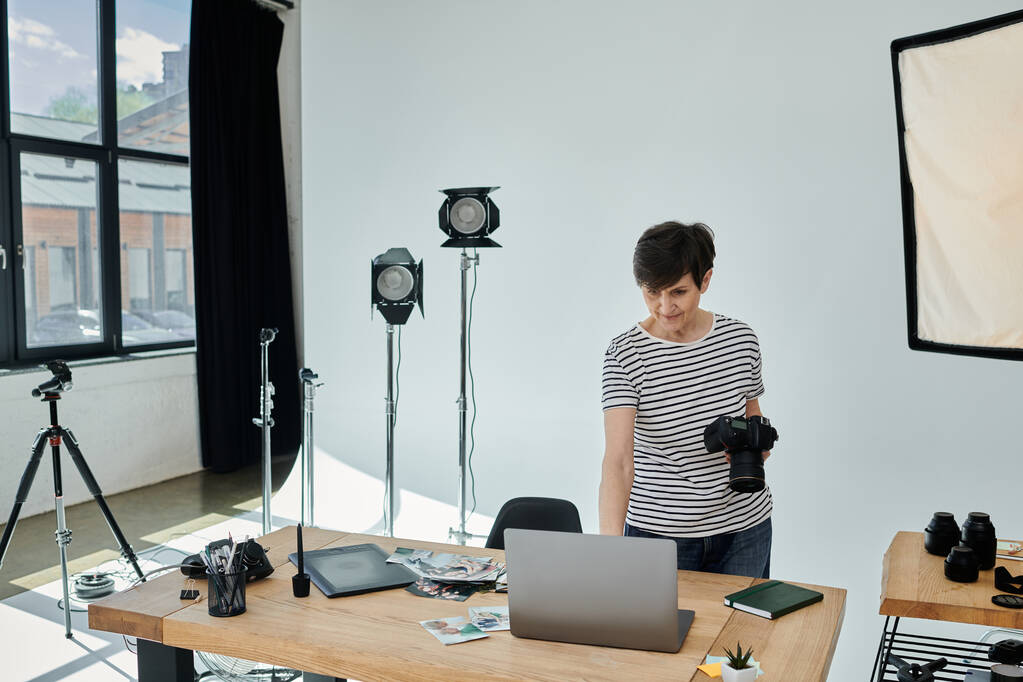 Жінка середнього віку стоїть впевнено, працюючи на ноутбуці в сучасному студійному просторі. - Фото, зображення
