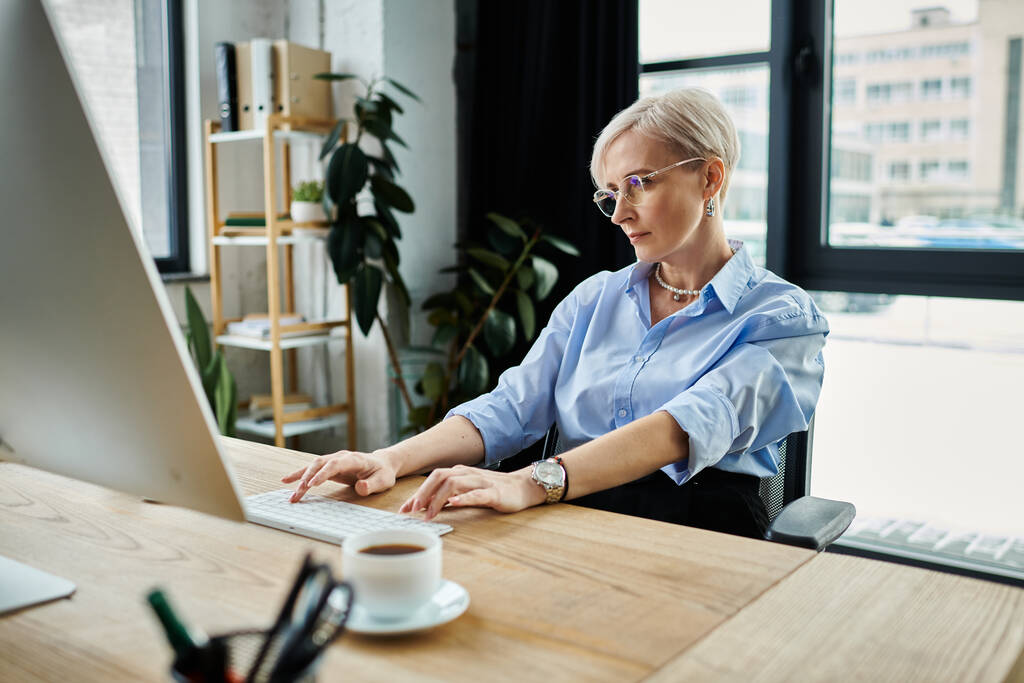 Une femme d'affaires d'âge moyen aux cheveux courts s'est concentrée sur son ordinateur portable pendant qu'elle travaillait dans un bureau pendant la ménopause. - Photo, image