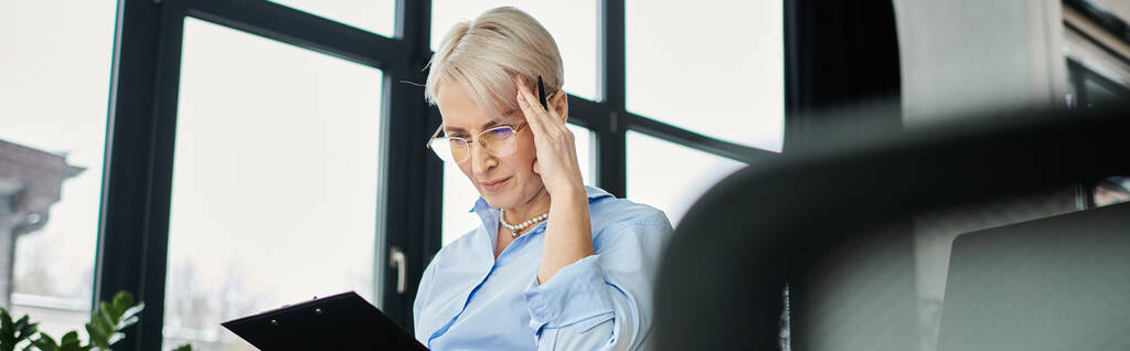 Obchodnice středního věku s krátkými vlasy viditelně zápasí, sedí za stolem s rukou na hlavě během menopauzy v kanceláři. - Fotografie, Obrázek