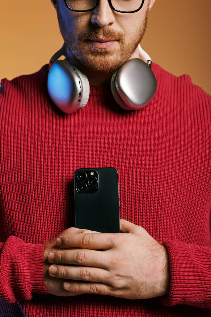 Un hombre con un atuendo elegante escucha música a través de auriculares mientras sostiene un teléfono celular. - Foto, Imagen