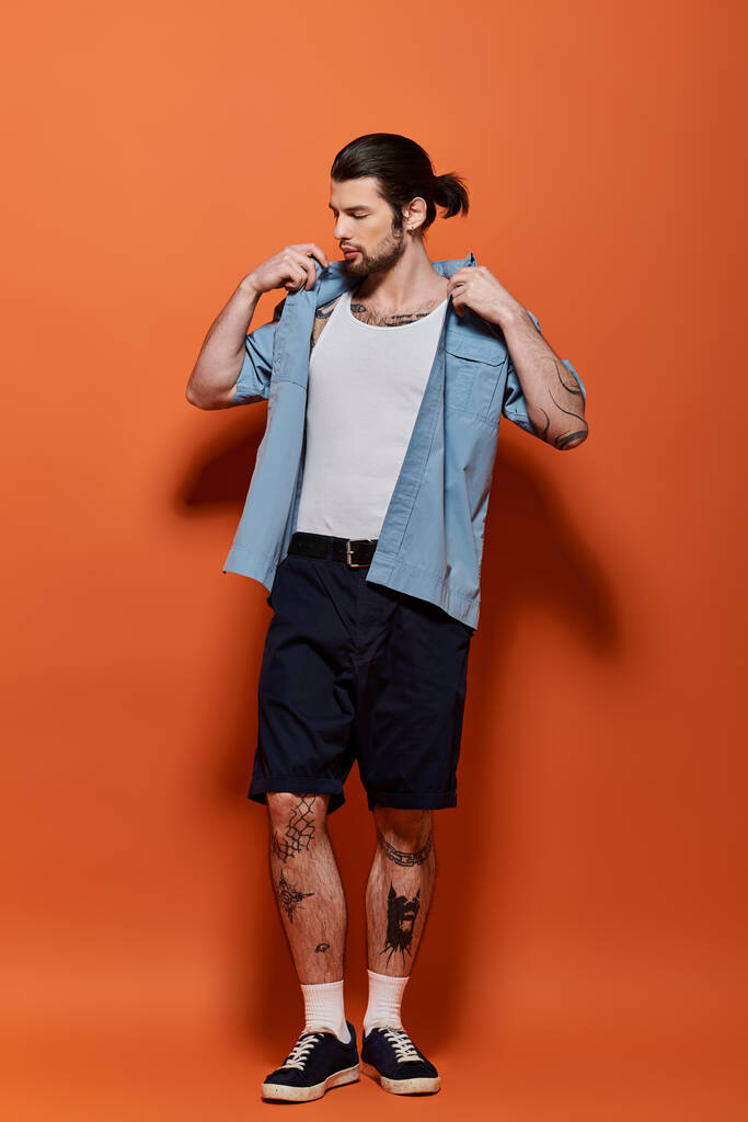 Hombre guapo con tatuajes de pie en traje de moda contra fondo naranja brillante. - Foto, Imagen