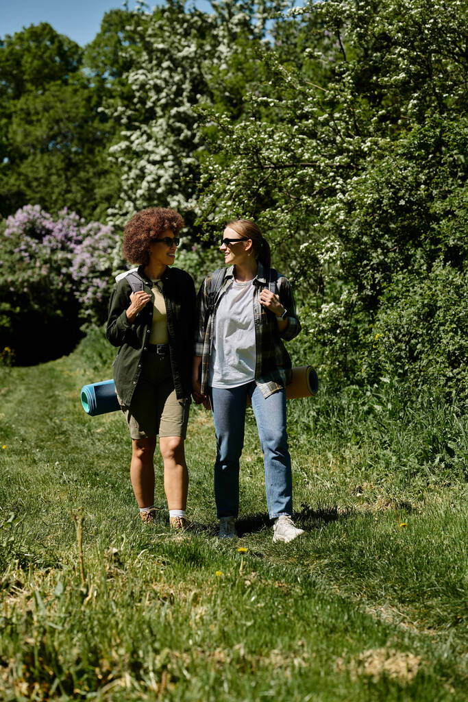 Két fiatal nő, egy leszbikus pár, együtt sétálnak egy buja zöld erdőben egy napsütéses napon.. - Fotó, kép