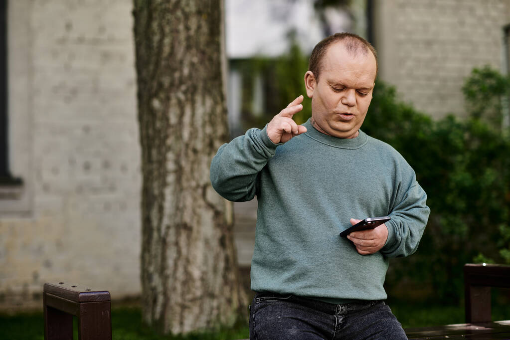 Человек с включённостью с телефоном в руке жестикулирует и разговаривает в парке. - Фото, изображение