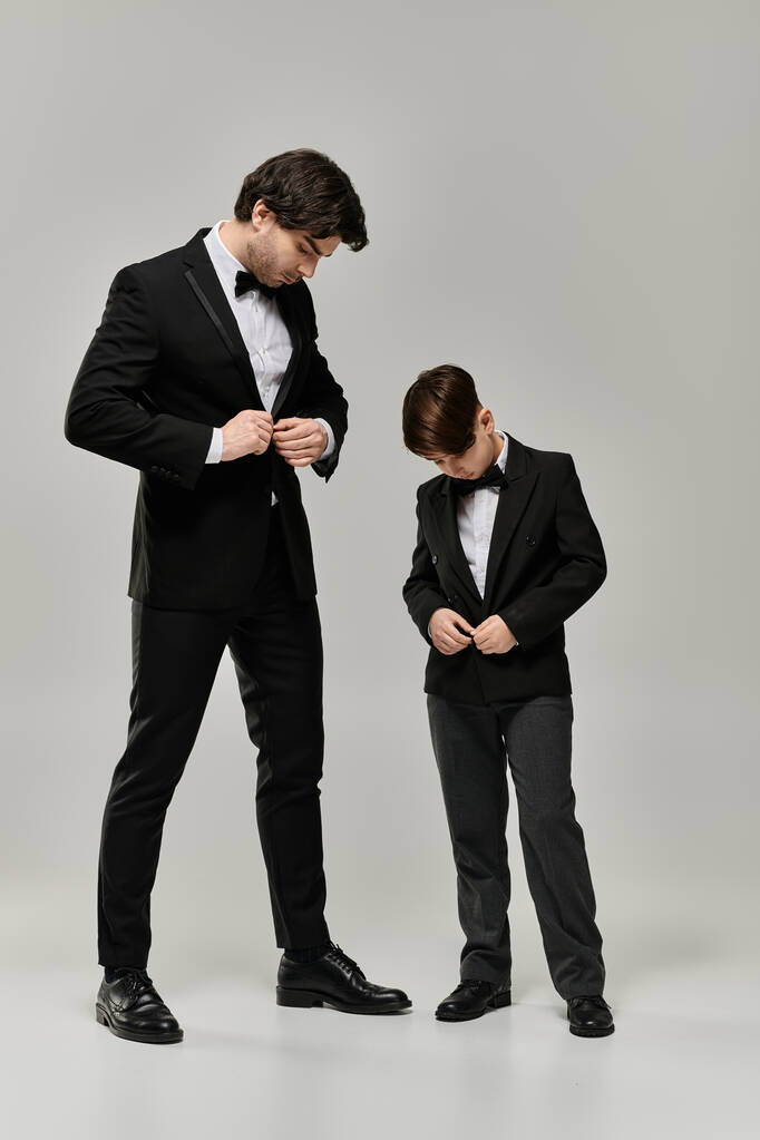Un padre y un hijo, ambos vestidos con esmoquin negro, están juntos en un ambiente de estudio. - Foto, Imagen