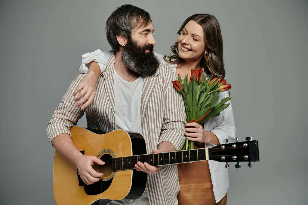 Una pareja posa junta, el hombre tocando una guitarra y la mujer sosteniendo un ramo de tulipanes. - Foto, Imagen