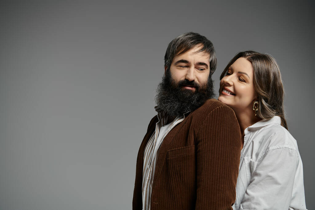 Una pareja cariñosa posa juntos, el hombre con una chaqueta de pana marrón y la mujer con una camisa blanca, sobre un fondo gris liso. - Foto, imagen