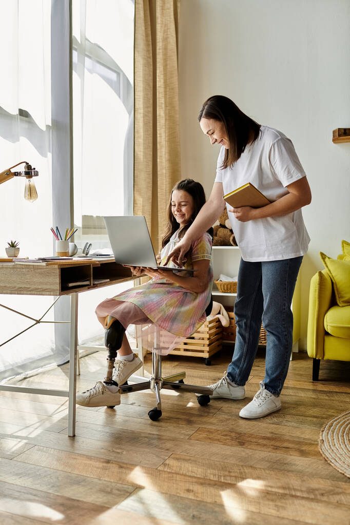 Une mère aide son enfant à utiliser un ordinateur portable à la maison. La fille a une prothèse de jambe. - Photo, image