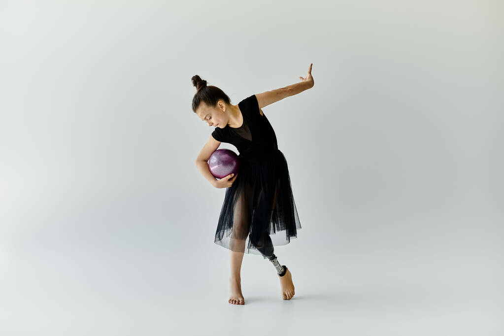 Ein junges Mädchen mit Beinprothese turnt mit einem lila Ball. - Foto, Bild