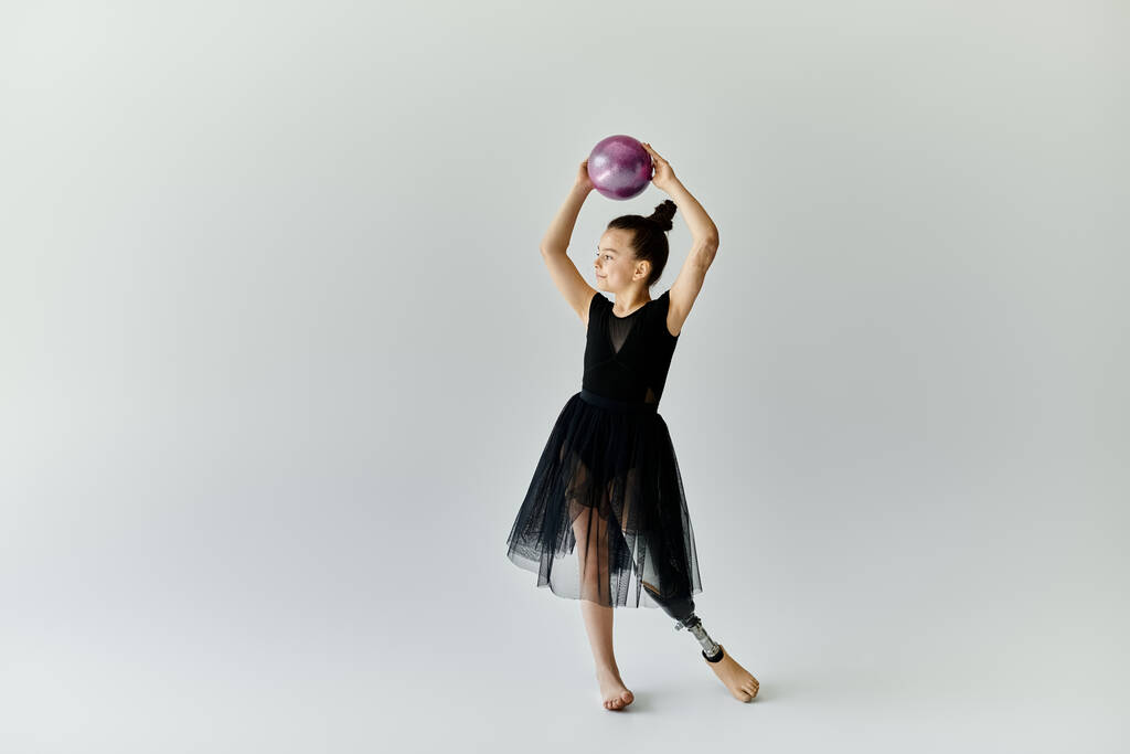 Молодая девушка с протезной ногой исполняет гимнастическую программу с мячом в студии. - Фото, изображение