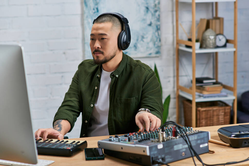 Komea aasialainen mies, joka käyttää kuulokkeita, soittaa musiikkia studiossaan, soittaa näppäimistöä ja miksauslautaa. - Valokuva, kuva