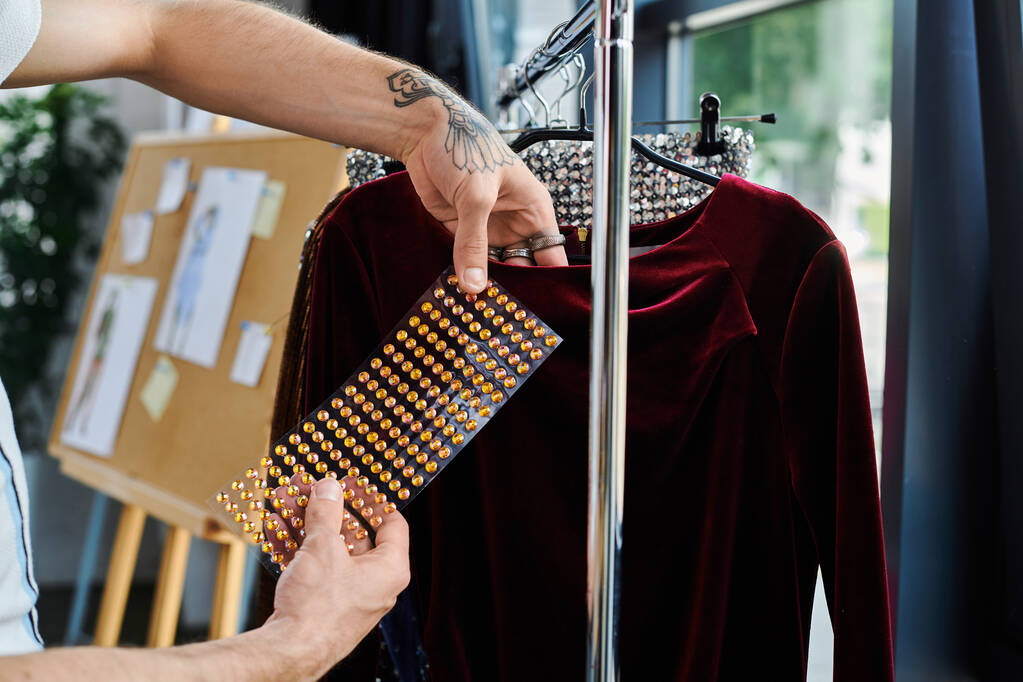 Młody człowiek ostrożnie umieszcza kryształy na aksamitnej sukni w swoim pracowni, pokazując swoje zaangażowanie w zrównoważoną odbudowę odzieży.. - Zdjęcie, obraz