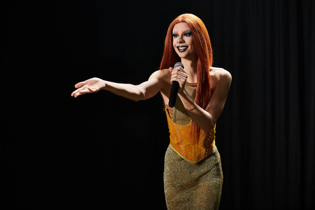 Una drag queen in un abito d'oro scintillante si esibisce sul palco, microfono in mano. - Foto, immagini