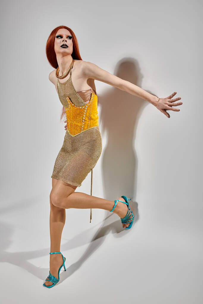 Een drag queen poseert in een glinsterende gouden jurk en turquoise hakken. - Foto, afbeelding