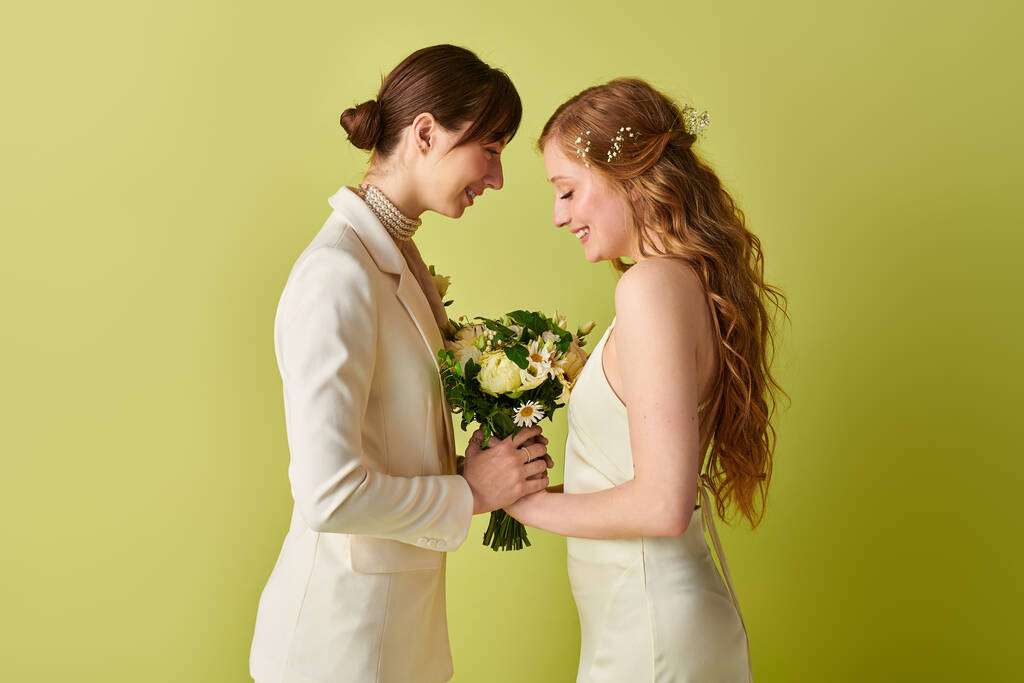 Beyazlar içinde genç bir lezbiyen çift düğün törenlerinde bir buket çiçek tutarken birbirlerine gülümsüyorlar.. - Fotoğraf, Görsel