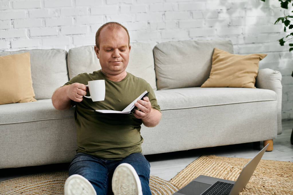 Чоловік з обмеженими можливостями відпочиває на підлозі вдома, насолоджуючись чашкою кави та книгою. - Фото, зображення