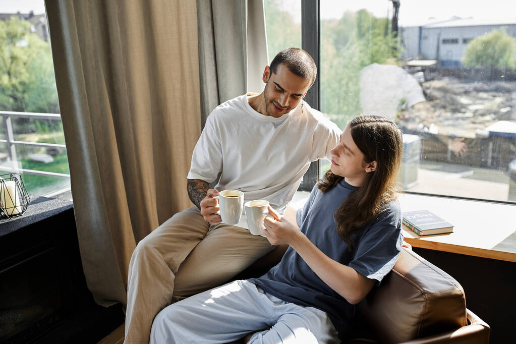 Mladý homosexuální pár si spolu vychutnává ranní kávu ve svém moderním domě, naplněném přirozeným světlem. - Fotografie, Obrázek