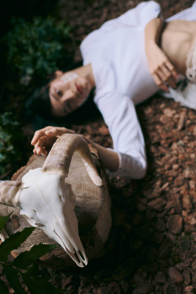 Una mujer yace en un bosque pantanoso, su mano descansando sobre un cráneo blanco. - Foto, imagen