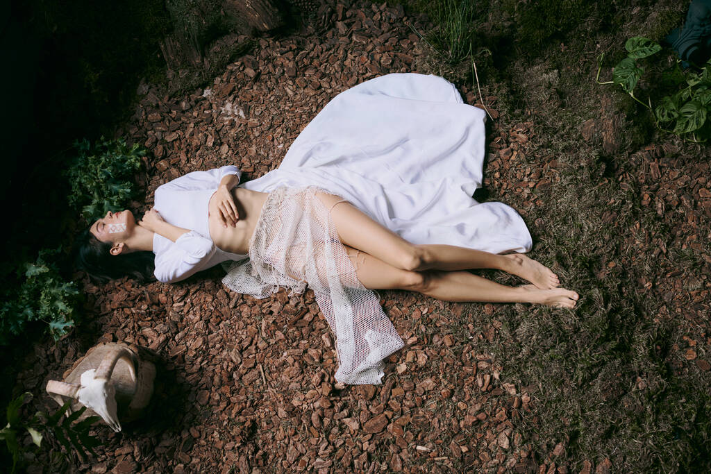 女性が森の掃除に横たわり,彼女の周りに白いドレスが流れています. - 写真・画像
