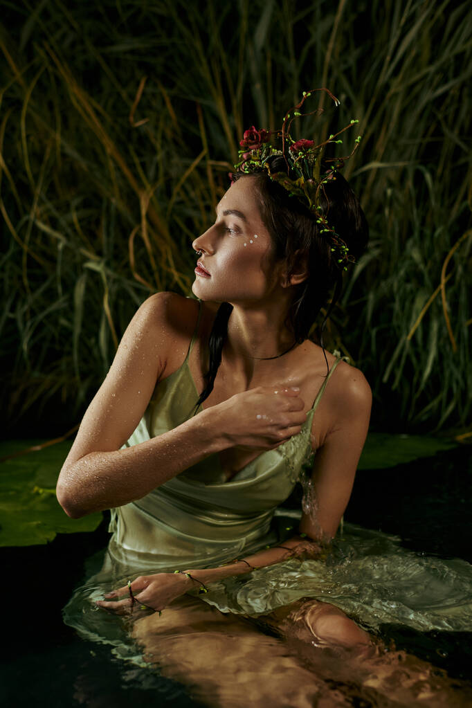 Una donna attraente, indossando una corona floreale, siede in una palude, guardando il cielo crepuscolare.. - Foto, immagini