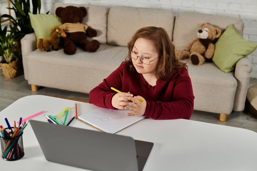 Маленька дівчинка з синдромом Дауна сидить за столом, розмальовуючи в блокноті. - Фото, зображення
