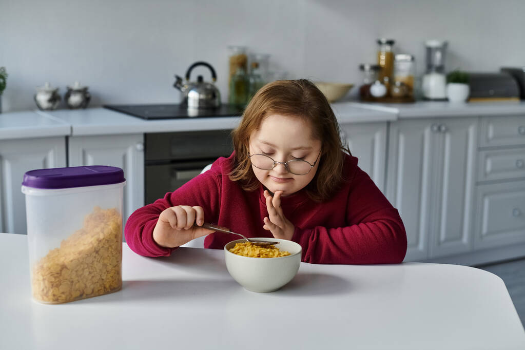 Una niña con síndrome de Down disfruta de un tazón de cereal en casa. - Foto, Imagen