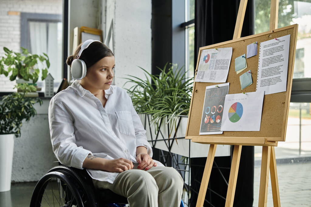 Молодая предпринимательница с ограниченными возможностями сидит в инвалидном кресле и работает в современном офисе. - Фото, изображение